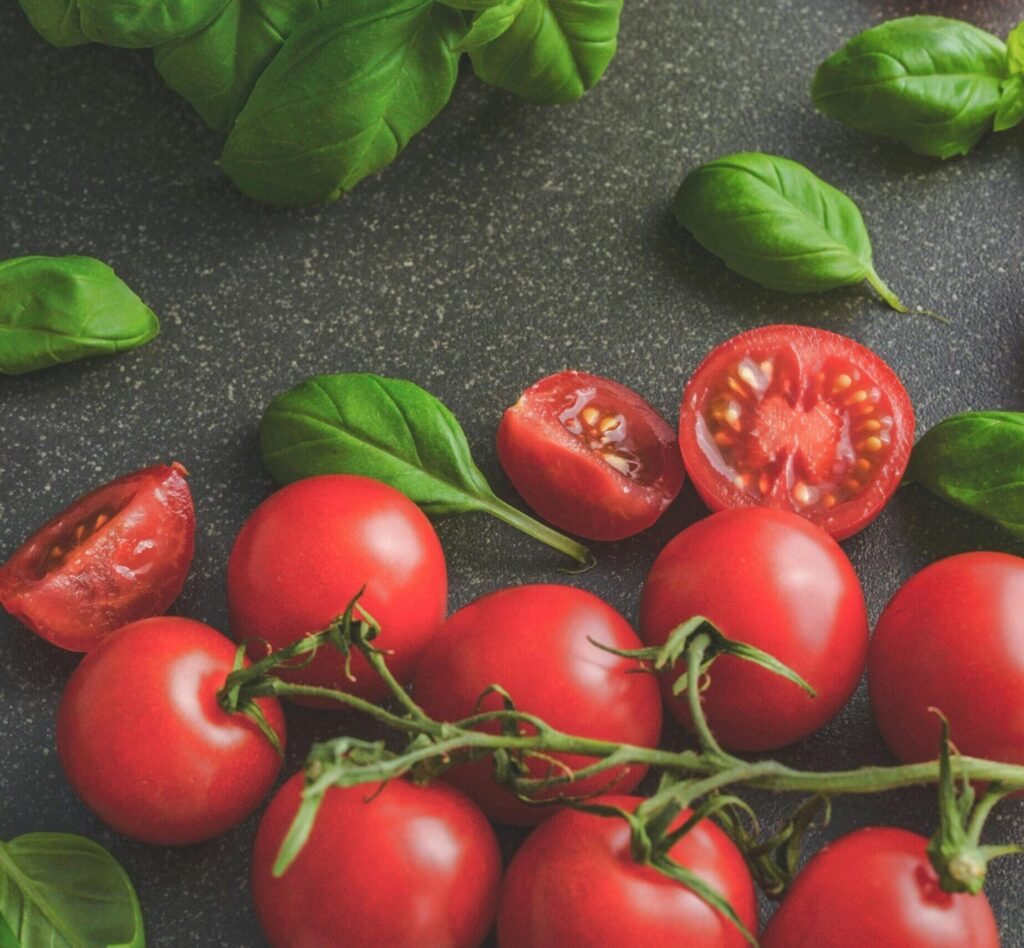 Organic basil leaves with ripe tomatoes on a rustic countertop, highlighting fresh ingredients for cooking.